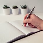 person holding silver retractable pen in white ruled book